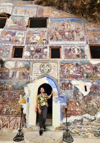 Sümela Manastırı Ana Kaya Kilisesi’nin dış cephesi; yoğun fresk programı ve kilise giriş kapısı önünde duran bir ziyaretçiyle birlikte genel görünüm.
